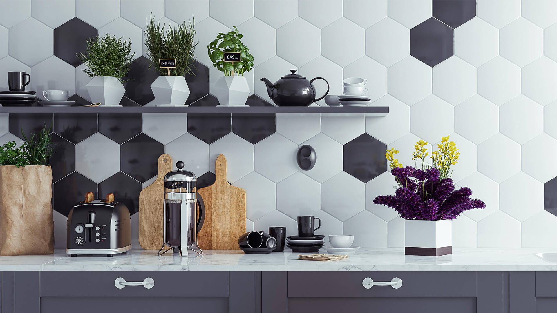 Grey and white hexagon tiled wall, with grey kitchen cabinets and silver appliances. Small herb plants and flowers on shelves.