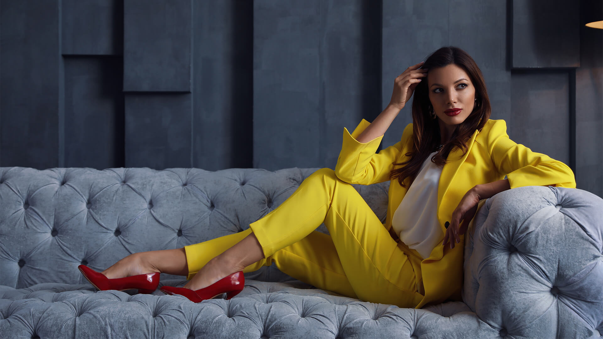 Female beauty CEO in a bright suit on a luxurious grey velvet sofa