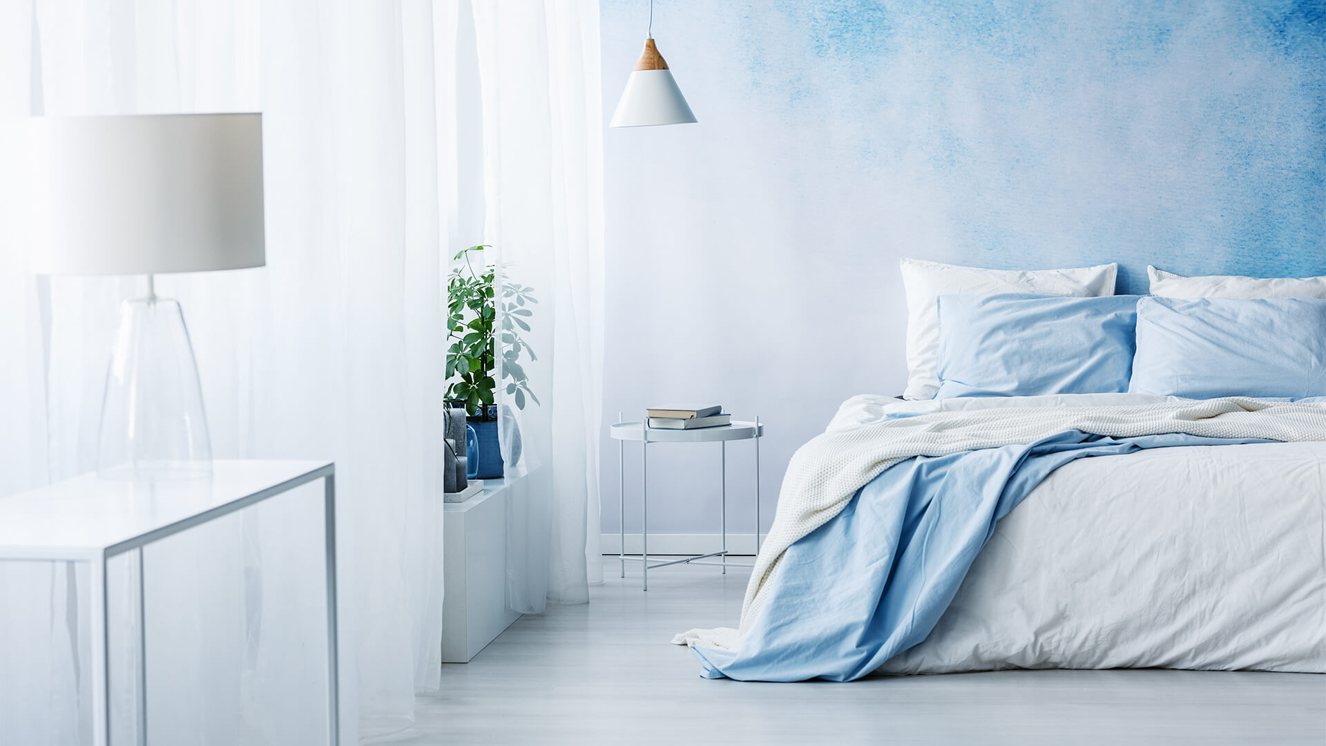 Bedroom interior with blue ombre wall, white bed with blue blanket, white lamp and table
