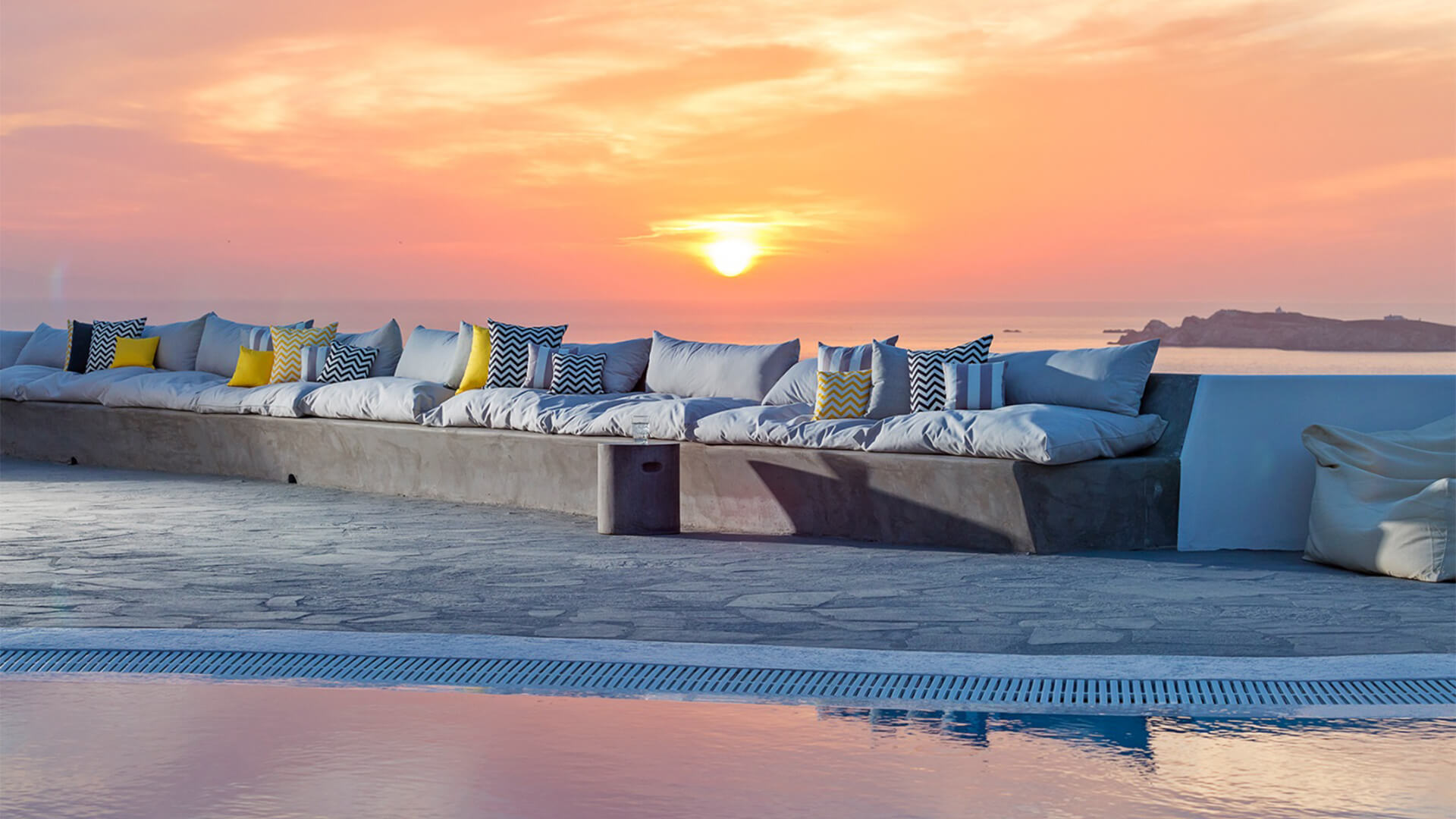 Stone seating area with cushions with a pink sunset behind