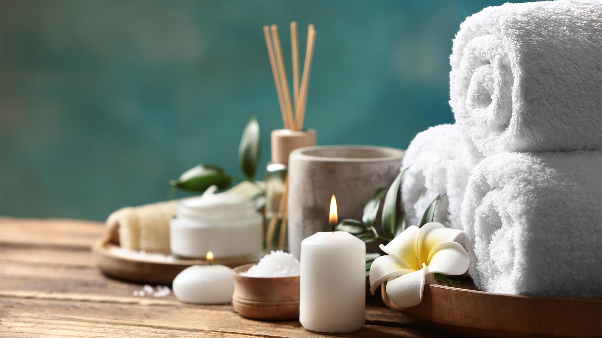 Rolled towels with fragrance sticks, candles, flowers on a wooden tray