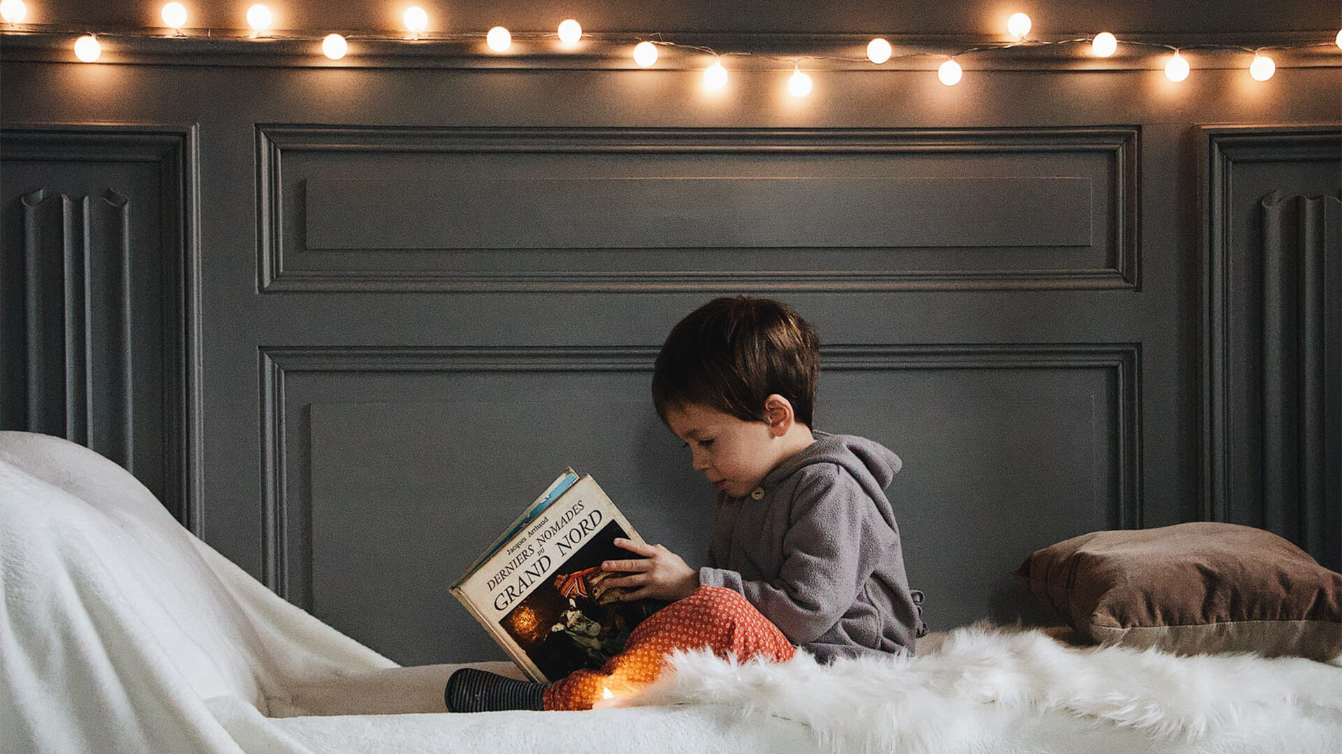 Kid reading alone in his room, with fairy lights in the wall behind him