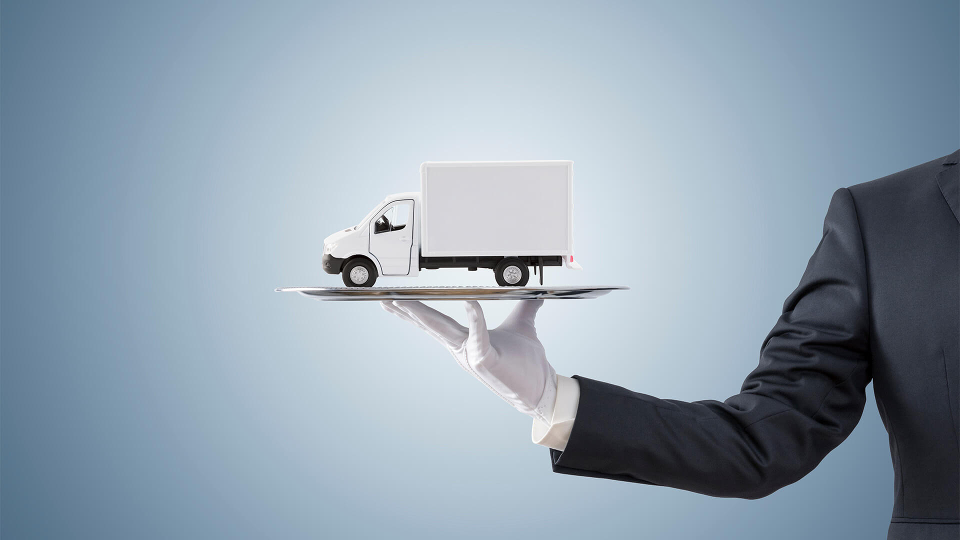 Butler with white gloves holding up a silver tray with a delivery van model on it
