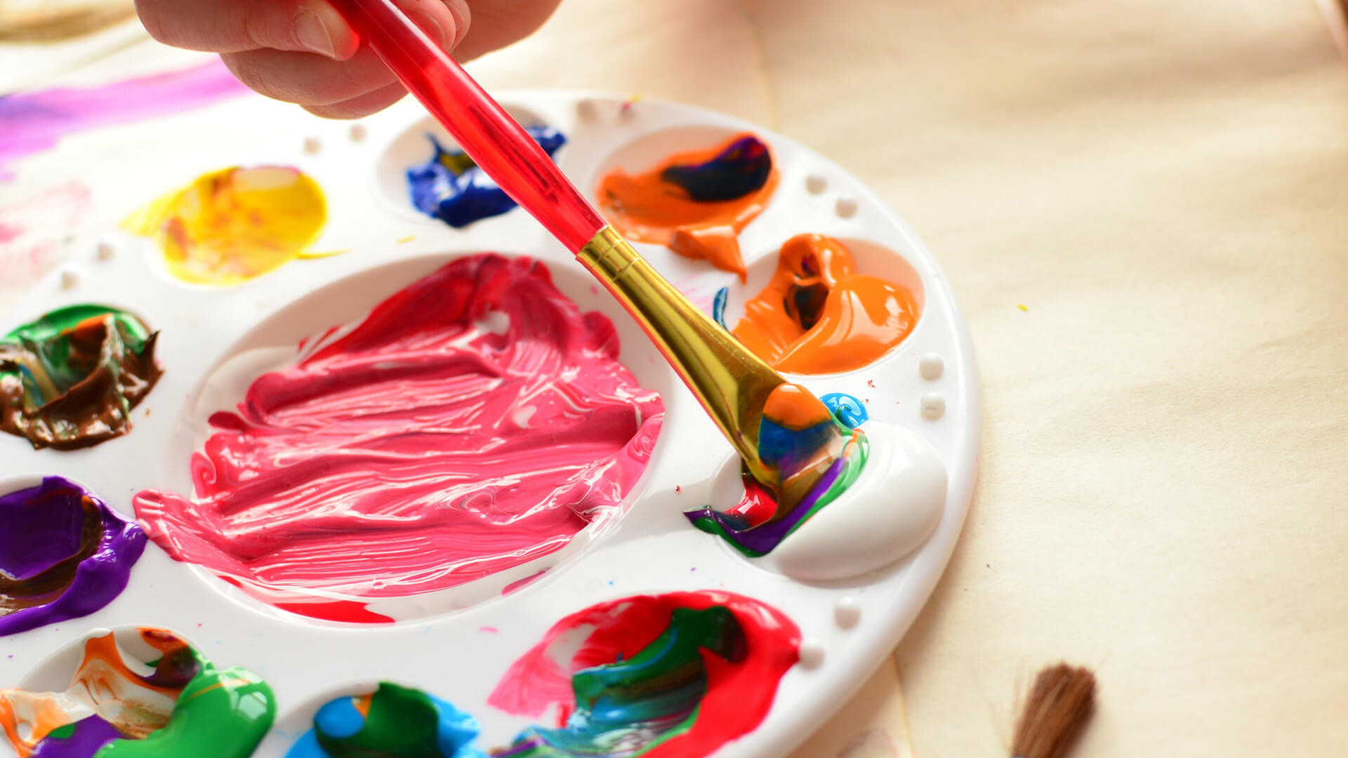 Closeup of a plastic painter's pallette with a child dipping a brush into the colours