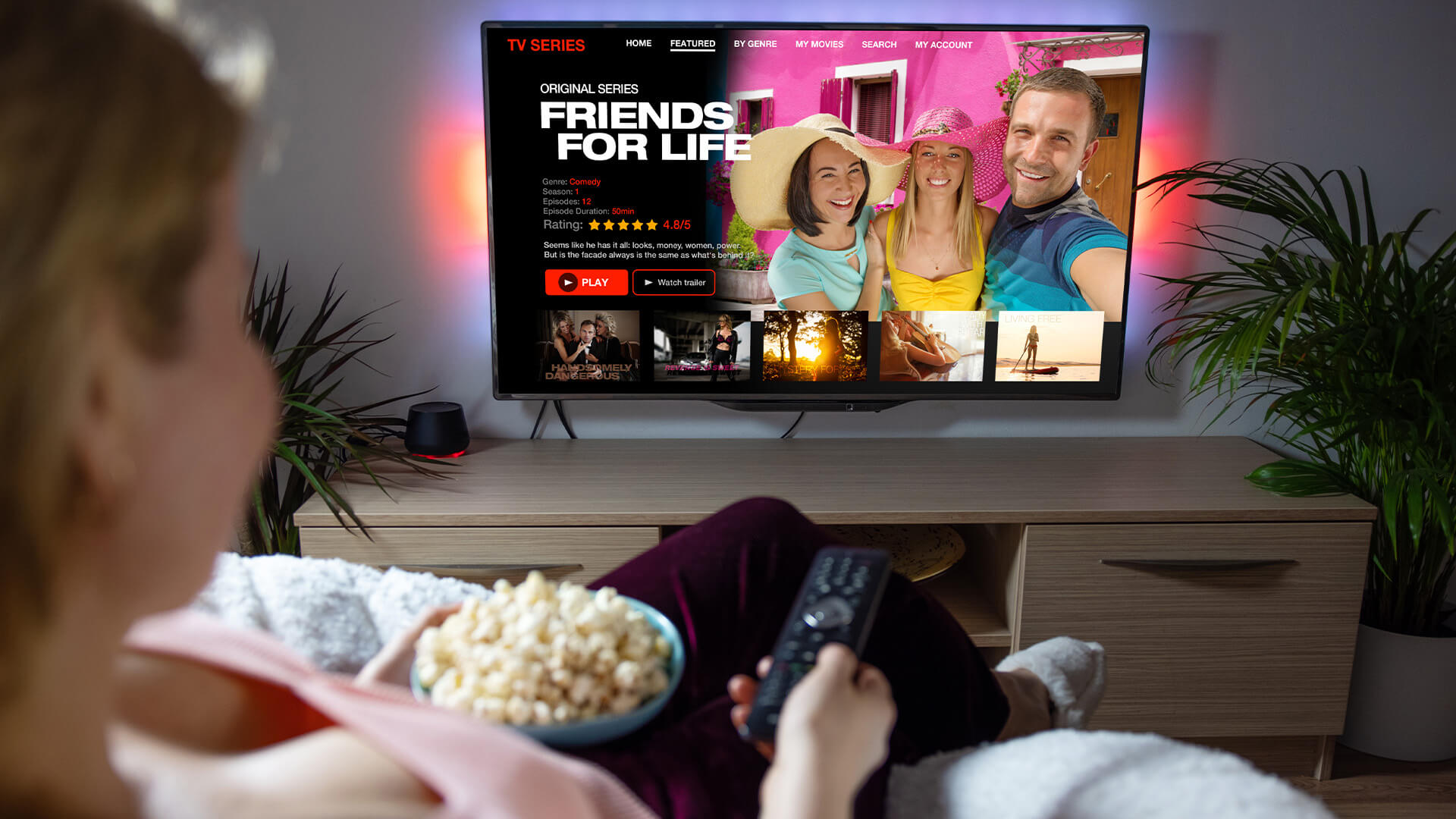 Woman watching a streaming service on her smart TV. She's on the sofa eating a bowl of popcorn with a remote in her hand