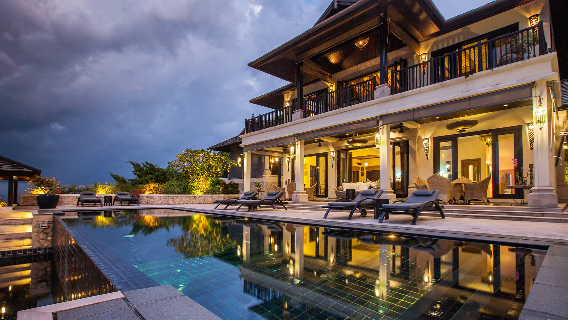 Exterior of a dark toned villa in the evening by a pool