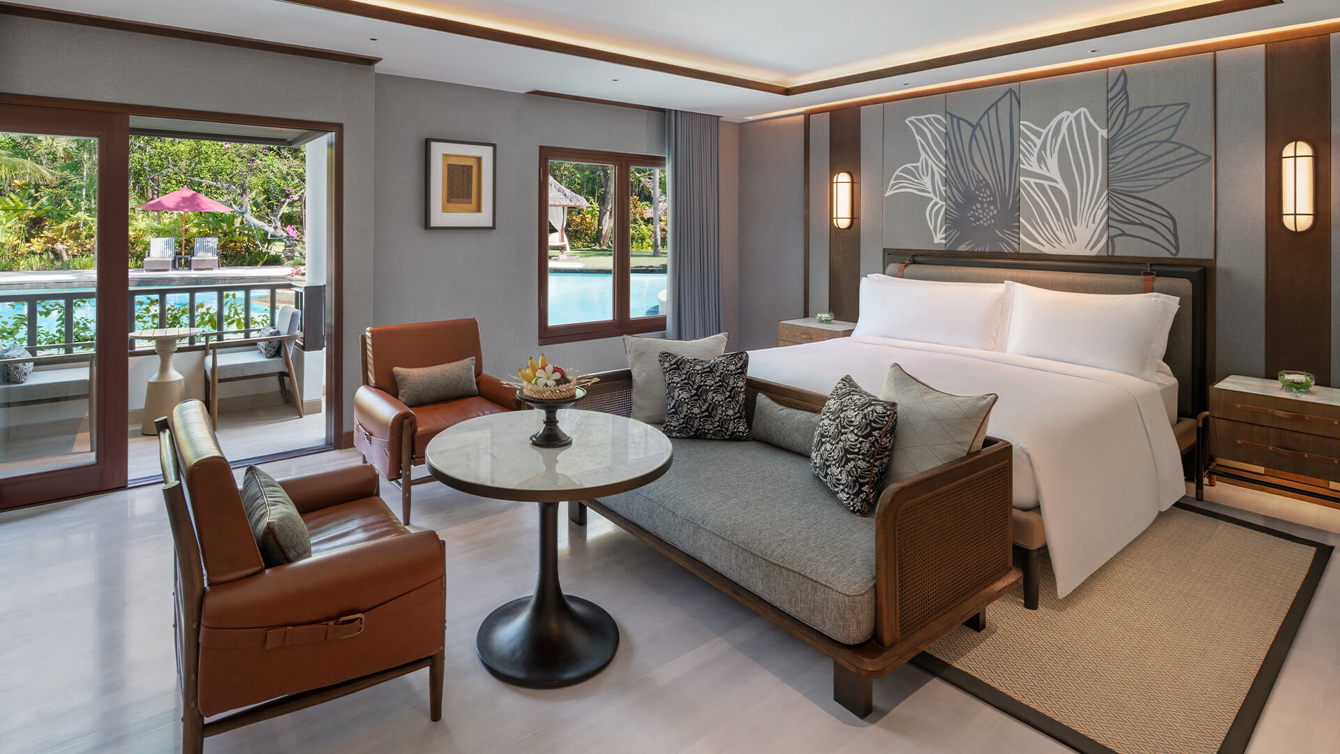 A Luxury studio room at The Laguna Resort showing a large bed, luxury seating with a small table and a view of the balcony and pool through the sliding doors