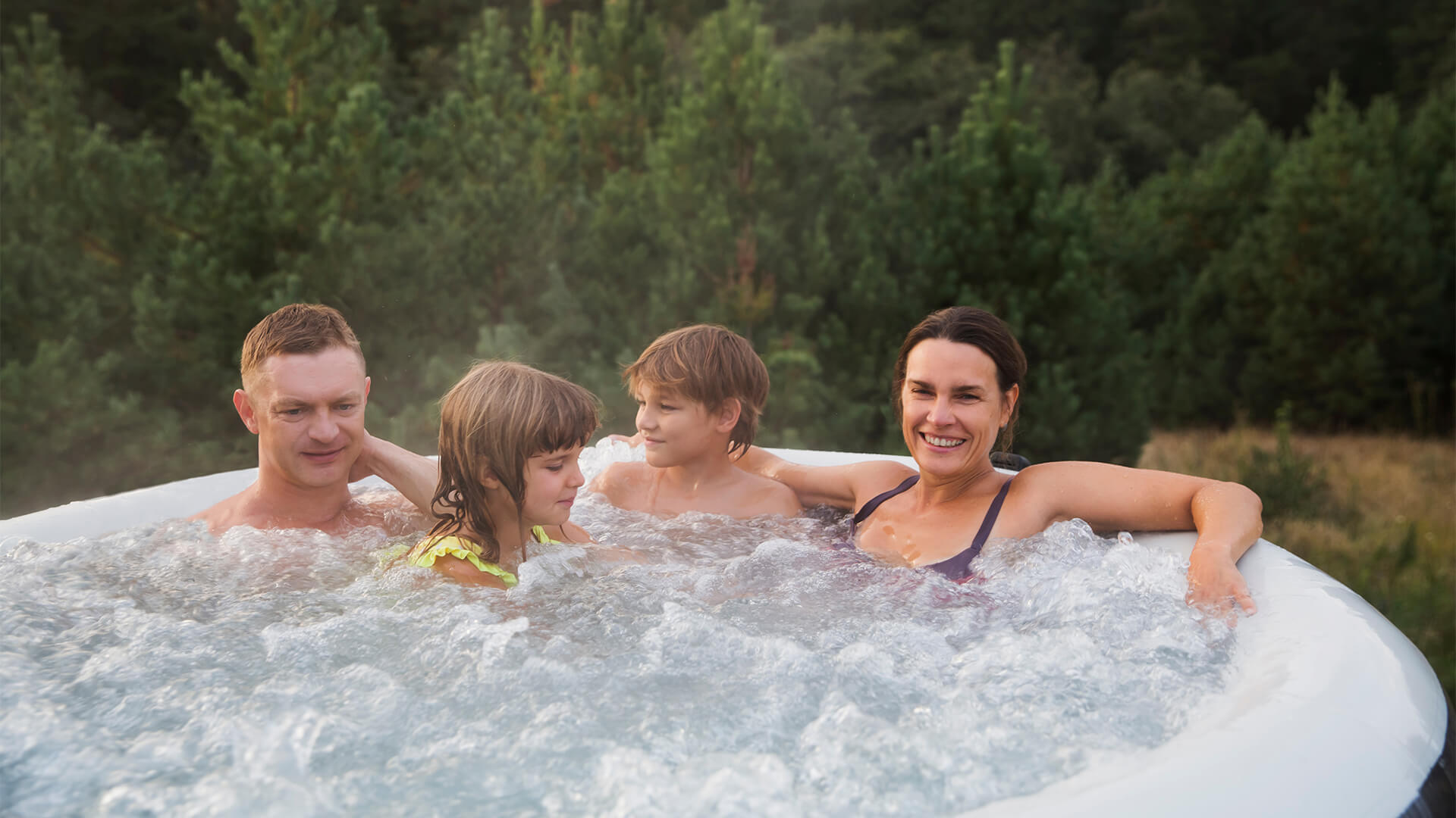 Family dad, mom and two kids rests in a hot tub in autumn cold weather against the background of green pine forest.