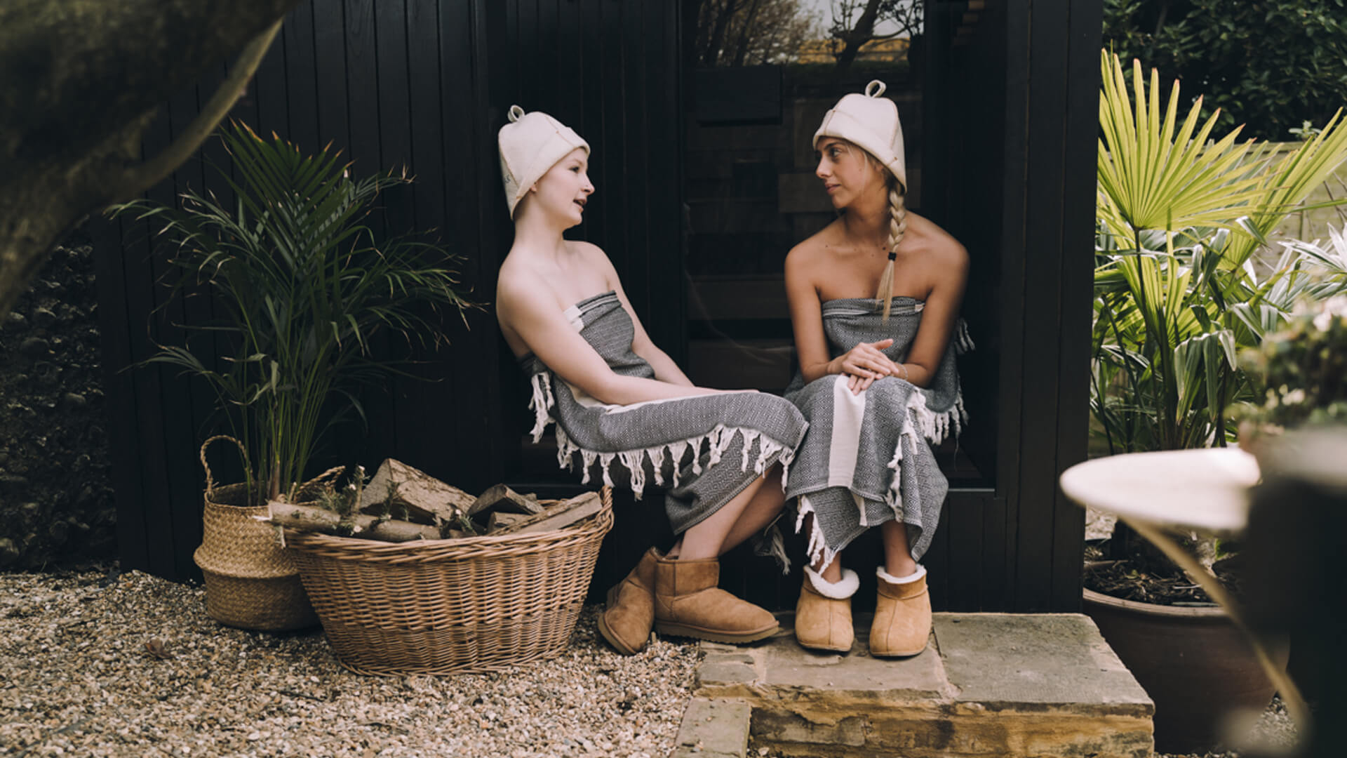 two women sat outside in hats and blankets wrapped around them