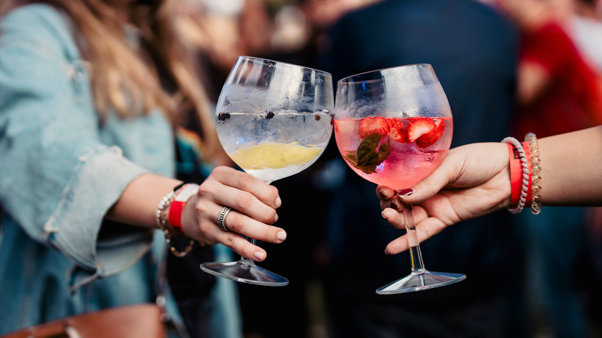 Two women holding a gin and tonic and toasting during a music festival