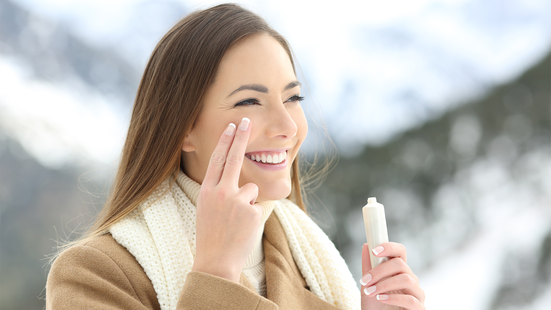 Happy lady applying facial moisturizer cream in winter