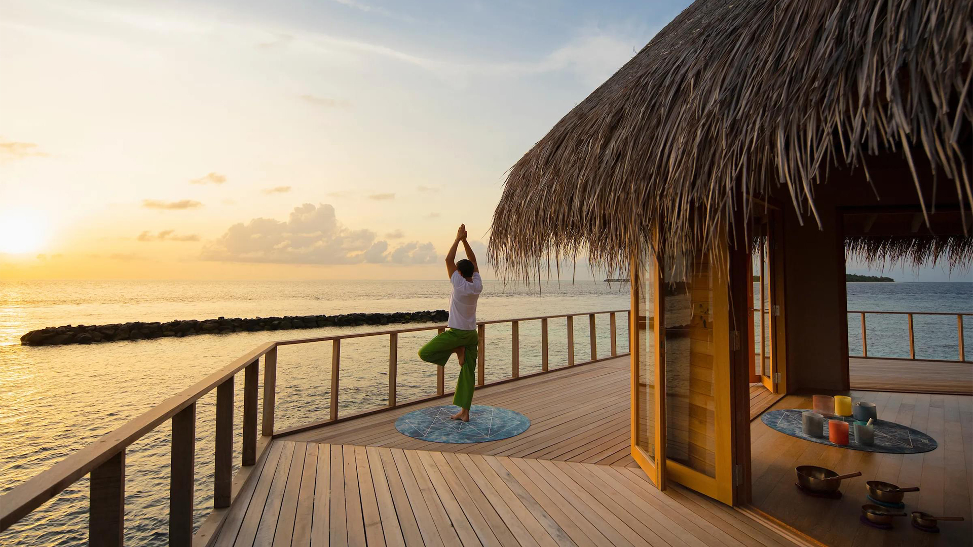 person doing yoga in front of the ocean in a hut balcony
